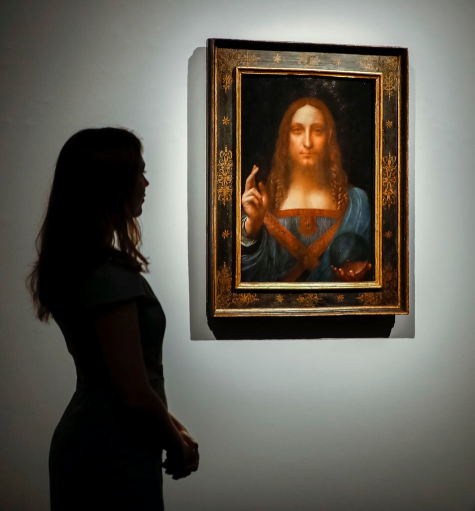 Christie's employees pose in front of a painting entitled Salvator Mundi by Italian polymath Leonardo da Vinci at a photocall at Christie's auction house in central London on October 22, 2017 ahead of its sale at Christie's New York on November 15, 2017. Photo courtesy Tolga Akmen/AFP/Getty Images.