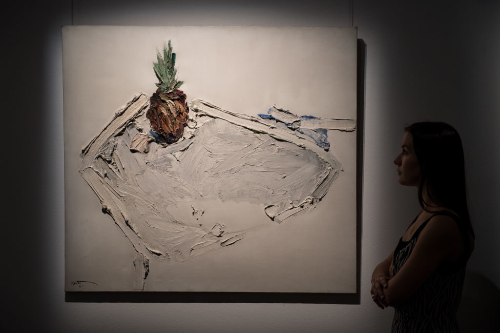 A Sotheby's employee poses next to 'Untitled (Still life with pineapple)' by Manoucher Yektai during a press preview of Orientalist and Middle Eastern Art Week at Sotheby's on April 20, 2018 in London, England. Photo by Chris J Ratcliffe/Getty Images for Sotheby's.