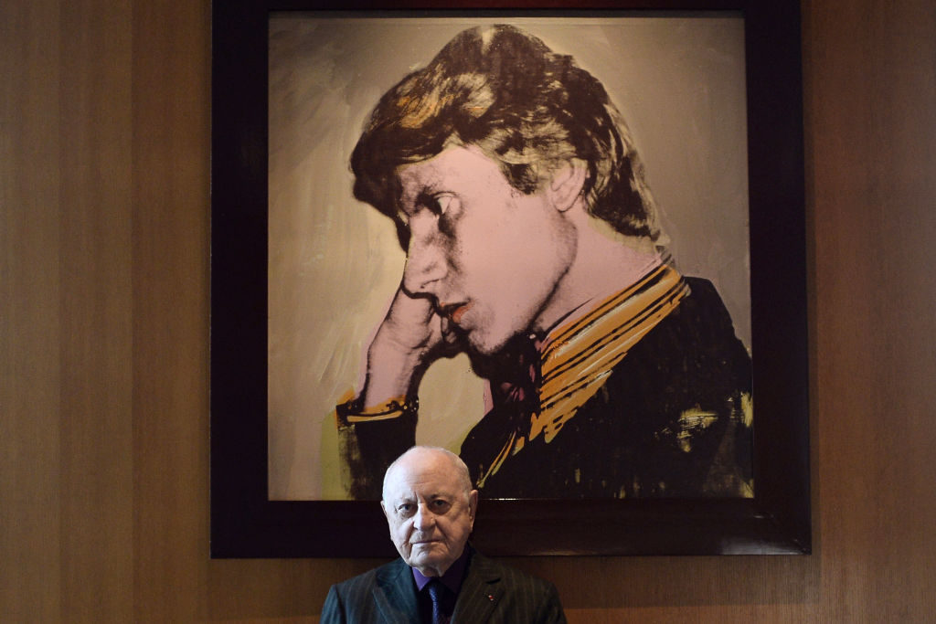 French businessman Pierre Bergé poses in front of a portrait of Yves Saint-Laurent by US artist Andy Warhol, on February 11, 2015 at his office in Paris. Photo courtesy Stephane de Sakutin/AFP/Getty Images.