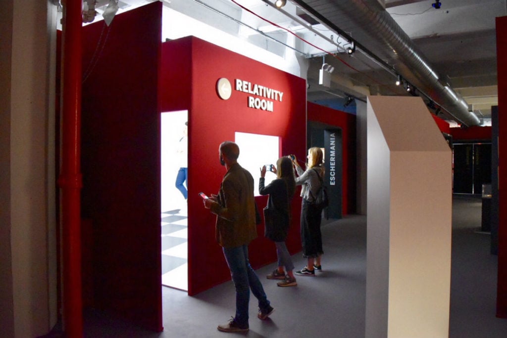 Visitors take photos in the "Relativity Room" in "Escher: The Exhibition & Experience." Image courtesy Ben Davis.