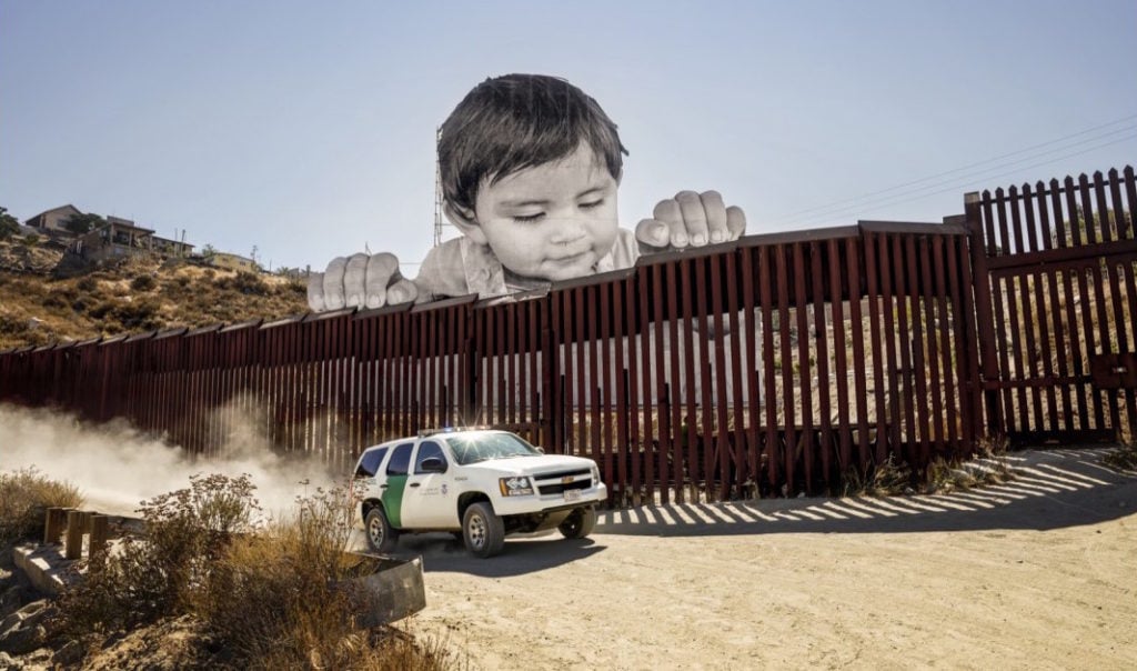 JR, <em>GIANTS, Kikito, September 7, 2017, 10:03 am, Tecate</em> (2017), a 65-foot photo of a Mexican child erected overlooking the border fence between the US and Mexico. Photo courtesy of Perrotin.