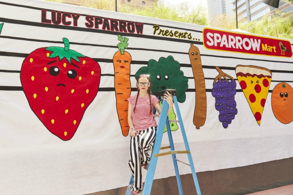 Lucy Sparrow with a mural she painted outside <em>Sparrow Mart</em>. Photo courtesy of the Standard.