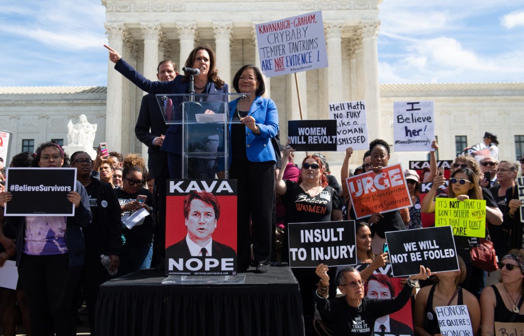 US Senator Kamala Harris, Democrat from California, US Senator Mazie Hirono, Democrat from Hawaii, and US Senator Richard Blumenthal, Democrat from Connecticut, all members of the Senate Judiciary Committee, speaks as demonstrators protest against Judge Brett Kavanaugh's nomination as an Associate Justice on the Supreme Court hold a rally outside the US Supreme Court in Washington, DC, September 28, 2018. Tracie Ching's <em>Kavanope</em> poster is prominently displayed against the podium. Photo by Saul Loeb/AFP/Getty Images.