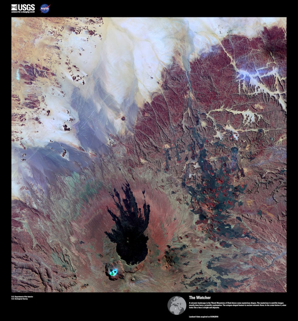Landsat 8, <em>The Watcher</em>. A volcanic landscape in the Tibesti Mountains of Chad shows some mysterious shapes. However, science can explain mysteries in satellite images. The octopus-shaped feature consists of ancient volcanic flows. In the crater below it, what looks like a face is bright salt deposits. Image courtesy of US Geological Survey/NASA.