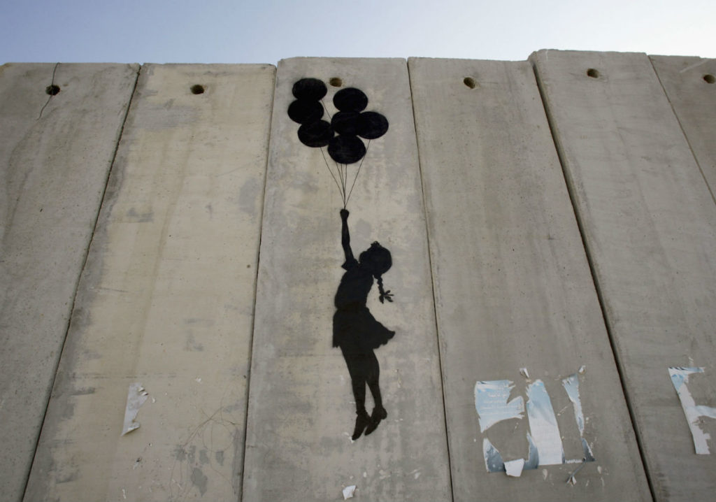 A graffiti titled <em>Balloon Debate</em> by Banksy, seen on August 6, 2005 on Israel's security barrier in Ramallah, West Bank. Photo by Marco Di Lauro/Getty Images.