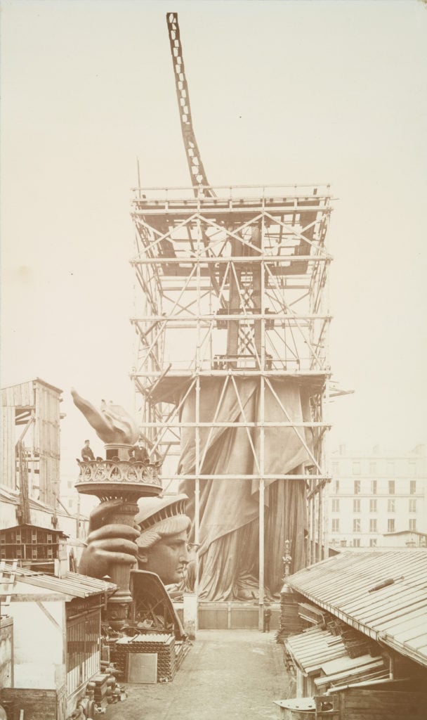 Assemblage of the Statue of Liberty in Paris, showing the bottom half of the statue erect under scaffolding, the head and torch at its feet (circa 1883). Photo by Albert Fernique, courtesy of the New York Public Library.