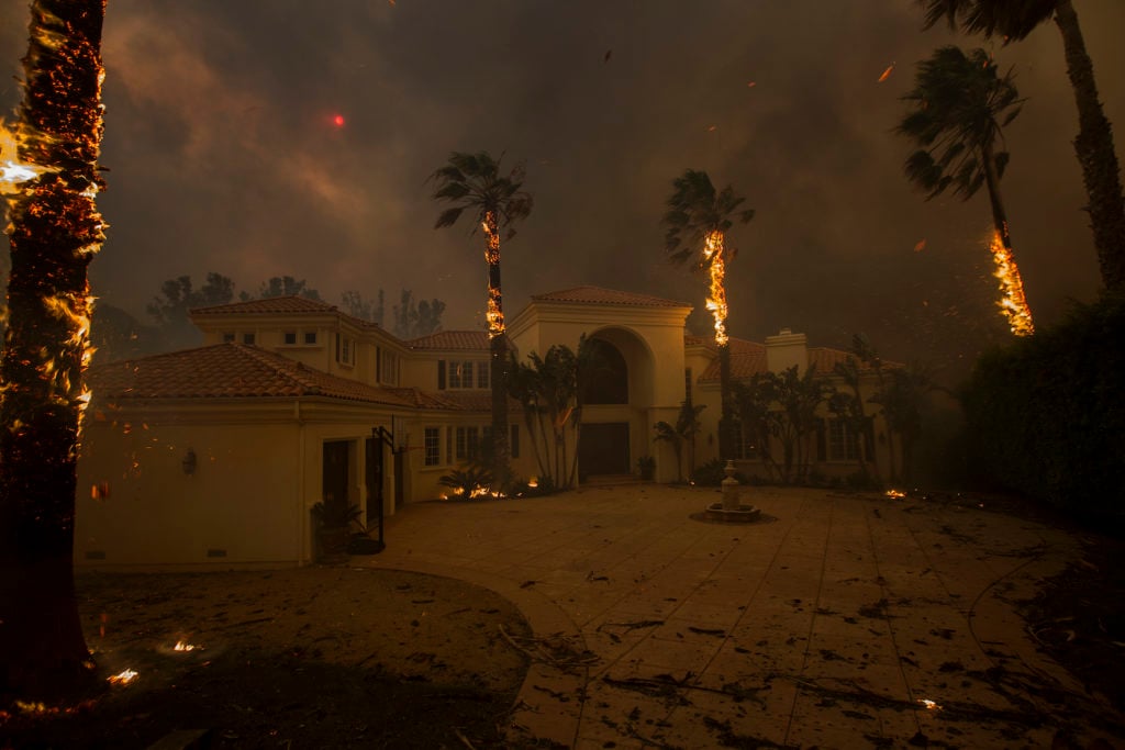 Embers falls from burning palms and the sun is obscured by smoke as flames close in on a house at the Woolsey Fire on November 9, 2018 in Malibu, California. Photo by David McNew/Getty Images.