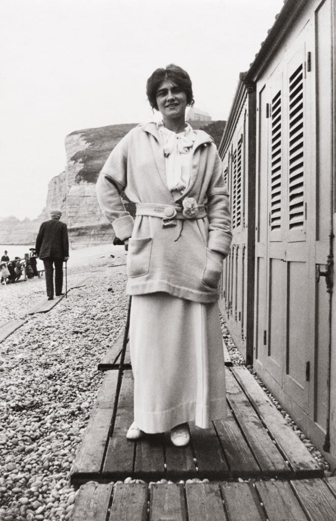 Gabrielle Chanel wearing a camellia pin on the beach at Étretat, around 1913. © Chanel.