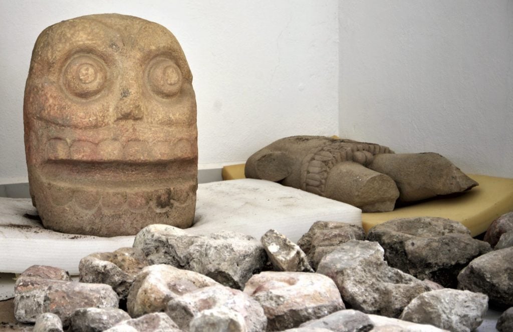 On the left, a skull-like stone carving depicting the Flayed Lord, a pre-Hispanic fertility god often shown as a skinned human corpse. It has been excavated from the Ndachjian-Tehuacan archaeological site in Tehuacan, Puebla. It is the first temple dedicated to the deity. Photo by Meliton Tapia Davila, courtesy of Mexico’s National Institute of Anthropology and History.