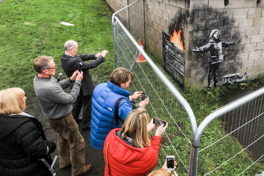 People gather around fences that have been erected to protect the latest piece of artwork by Banksy in Port Talbot, Wales. Photo by Matt Cardy/Getty Images.
