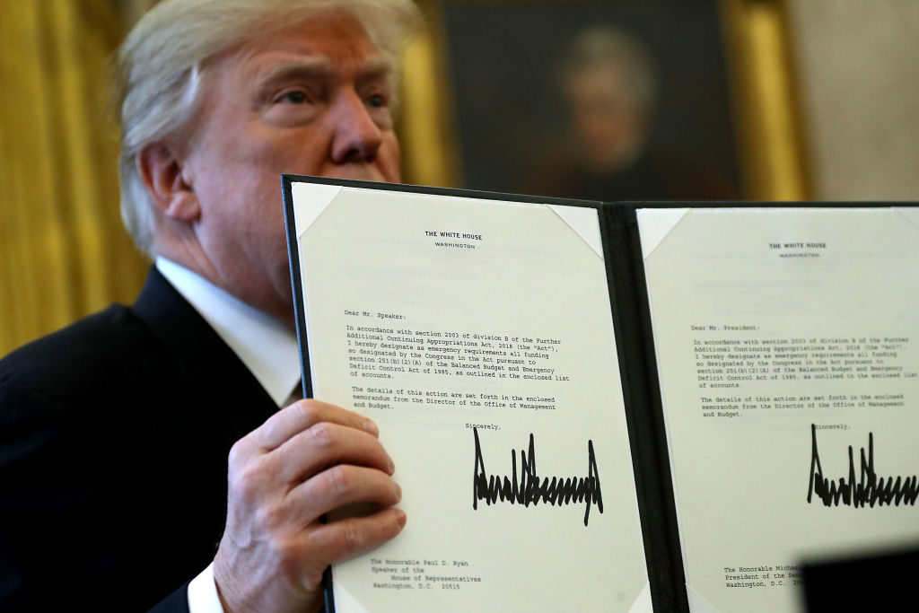 Donald Trump holds up a copy of legislation he signed before before signing the tax reform bill into law in the Oval Office December 22, 2017. Photo by Chip Somodevilla/Getty Images.