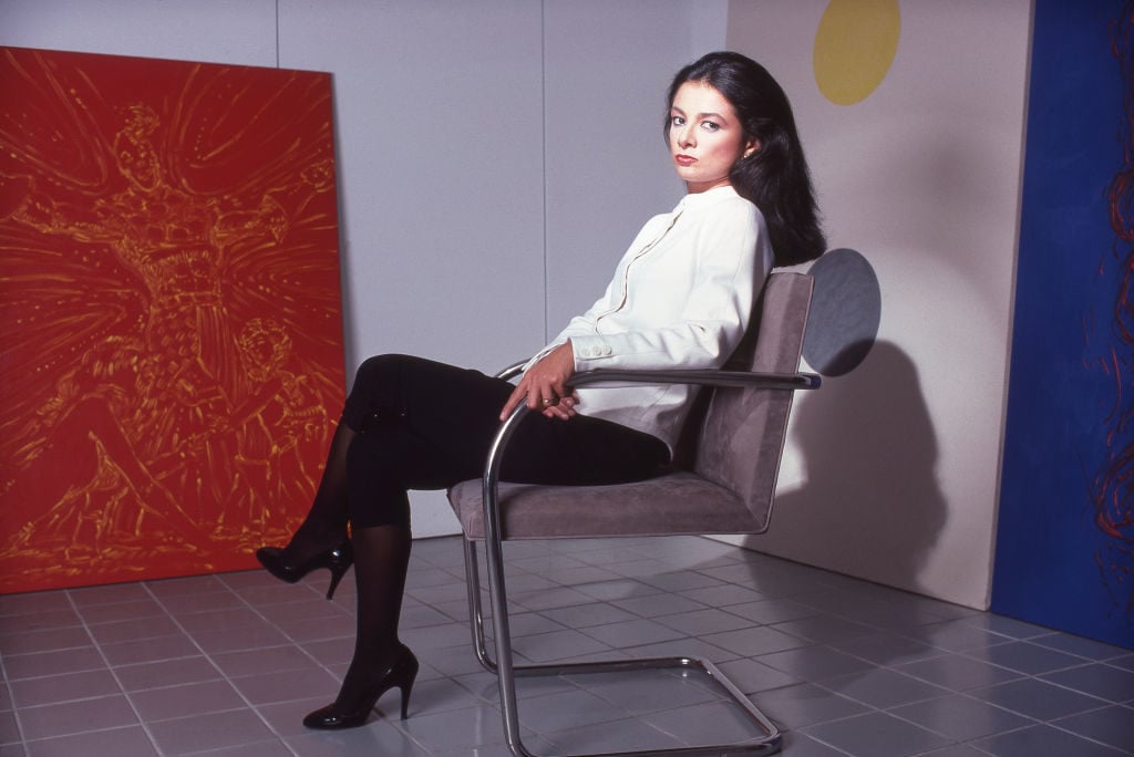 Art dealer Mary Boone reclines in a chair surrounded by paintings.