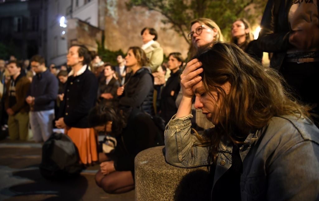People kneel on the pavement as they pray outside watching flames engulf Notre-Dame Cathedral in Paris on April 15, 2019. (Photo by ERIC FEFERBERG / AFP) (Photo credit should read ERIC FEFERBERG/AFP/Getty Images)