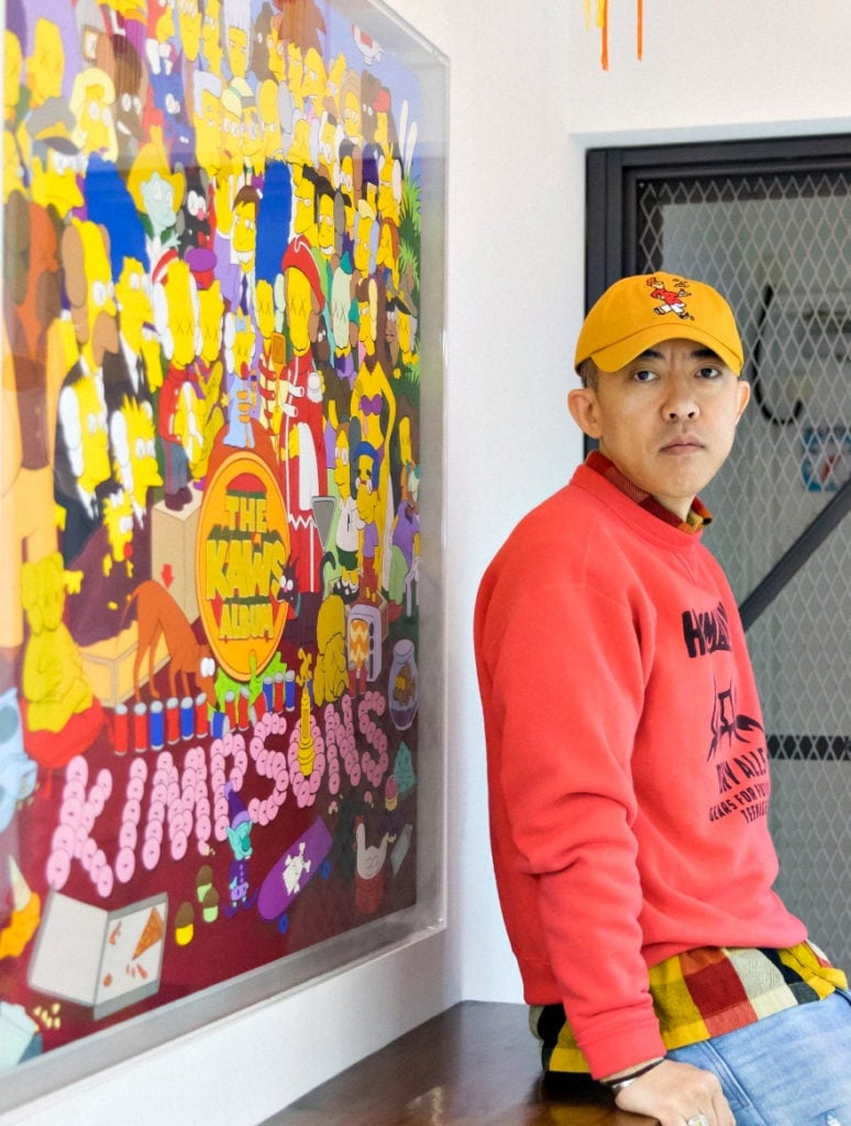 Collector NIGO with his KAWS painting <em>THE KAWS ALBUM</em>, which he sold for $14.8 million at Sotheby's Hong Kong. Photo by Thomas Thompson, courtesy of Sotheby's.