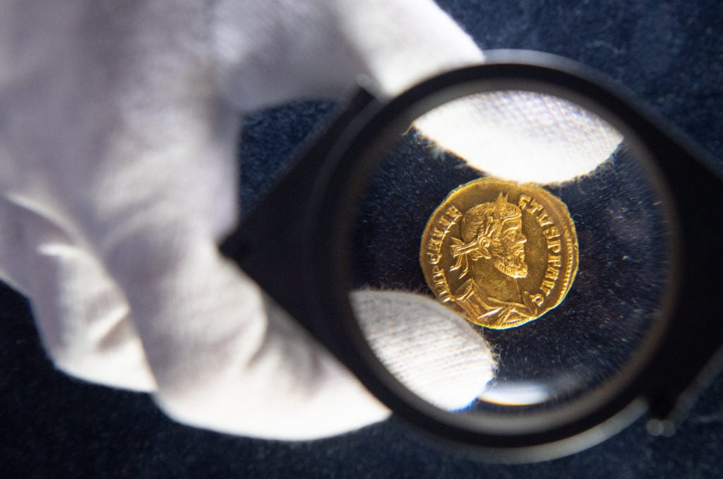 An employee of Dix Noonan Webb auction house holds a Roman coin dating from dating from AD 293-296, which was discovered in a Kent field. Photo: Dominic Lipinski/PA Images via Getty Images.