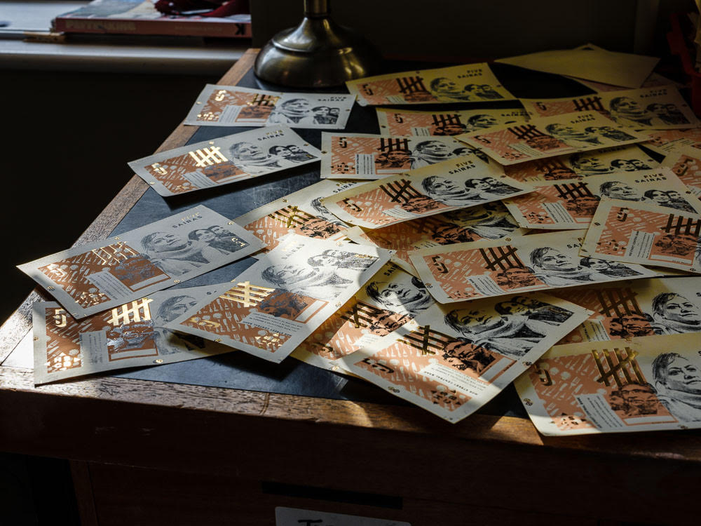 A table full of Daniel Edelstyn and Hilary Powell's alternative currency inside the Hoe Street Central Bank (HSCB). Photography by Peter Searle. Courtesy of the artists.