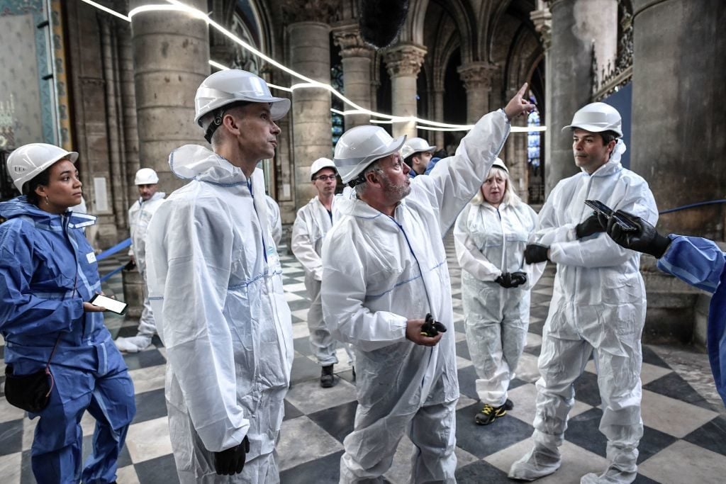 French Culture Minister Franck Riester (R) speaks with French chief architect of historical sites Philippe Villeneuve (L) as they visit the Notre-Dame de Paris Cathedral during preliminary work three months after a major fire. Photo by Stephan de Sakutin/AFP/Getty Images.