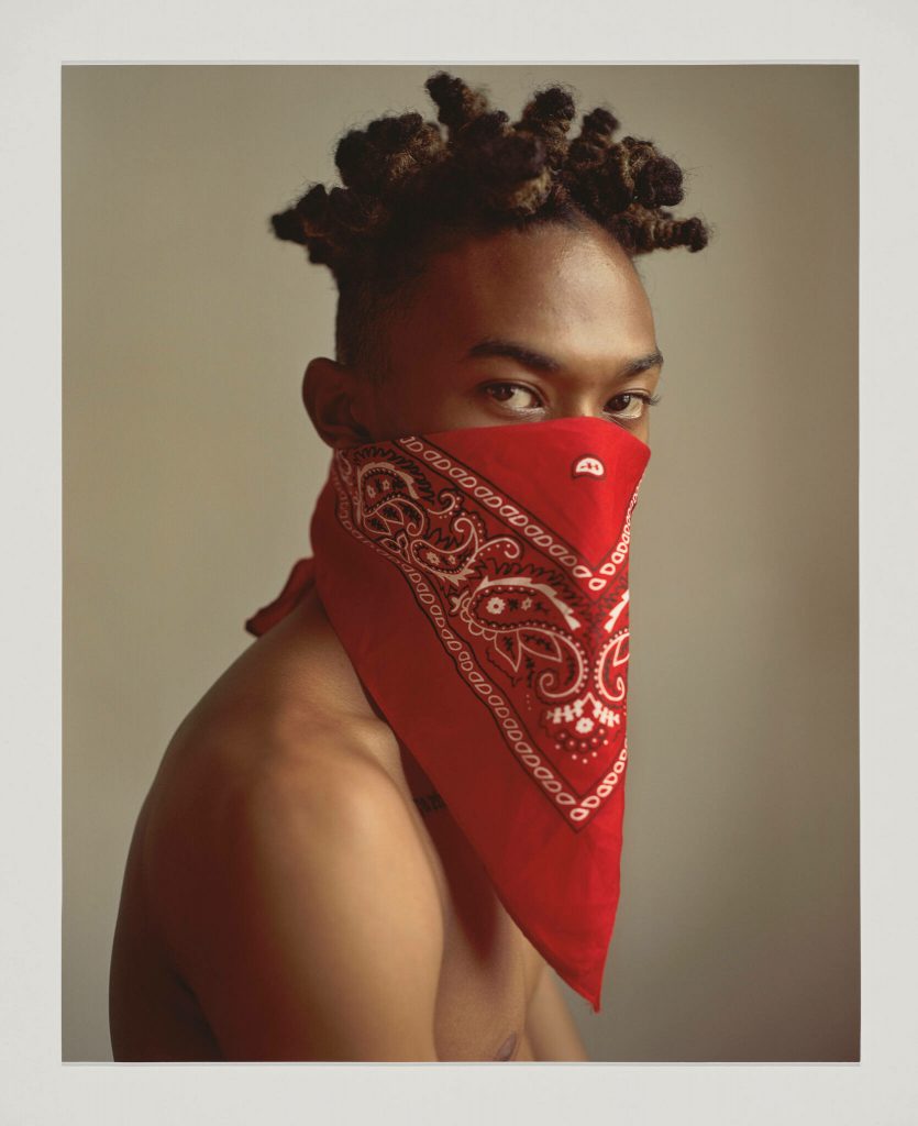 A Black man stares at the camera with a red bandana covering the bottom half of his face.