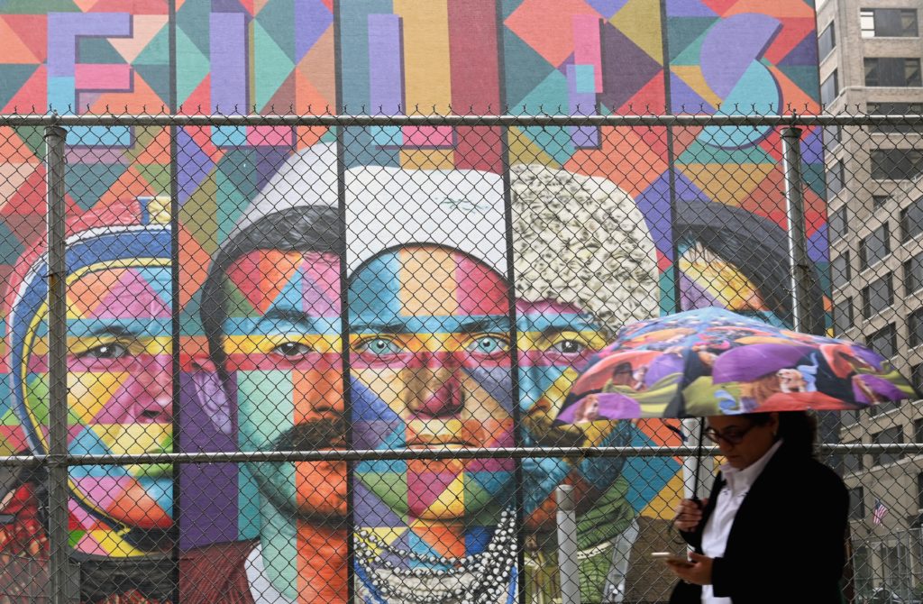 A woman with an umbrella walks past a mural named "Ellis Island" painted by artist Eduardo Kobra, on June 19, 2019 in New York City. Photo: Angela Weiss/AFP/Getty Images.
