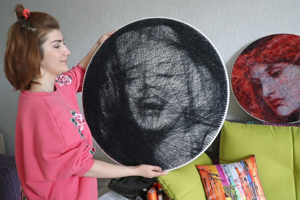 Artist Ani Abakumova holds a string art portrait of Marilyn Monroe in her workshop in the village of Romashkovo. Ani Abakumova and her husband Andrei Abakumov create string art replicas of famous paintings; Andrei makes computer calculations that show patterns for future images, then Ani winds colored strings around nails hammered around a plywood board. Photo by Anton Novoderezhkin/TASS/Getty Images.