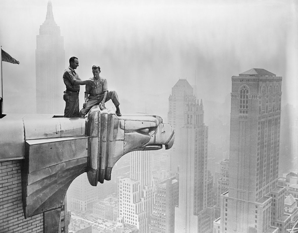 A man lights a fellow worker's cigarette as they take a break on a Chrysler Building gargoyle. Courtesy of Getty Images.