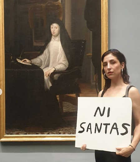 Artist Anastasia Bengoechea posed at the Museo del Prado in Madrid with Guido Reni’s Cleopatra and the Juan Carreño de Miranda portrait Queen Mariana of Austria with signs that translate to 