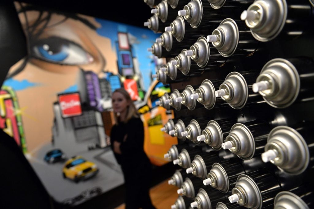 A wall of spray paint cans constructed for the exhibition "City as Canvas: GraffitiArt from the Martin Wong Collection" is seen with <em>Reflections on Times Square #2</em> (2013) by Chris "DAZE" Ellis at the Museum of the City of New York February 3, 2014 in New York. Photo courtesy Stan Honda/AFP/Getty Images.