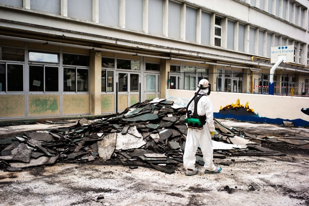 A worker stands next to asphalt waste materials as he takes part in a clean-up operation at Saint Benoit school near Notre-Dame cathedral in Paris during a decontamination operation over lead poisoning fears on August 8, 2019. Paris officials moved on August 6, 2019 to downplay the risk of lead poisoning from the massive fire that tore through Notre-Dame cathedral in April, as tests continue to show worrying levels of the toxic metal at nearby schools. Photo by Martin Bureau/AFP/Getty Images.