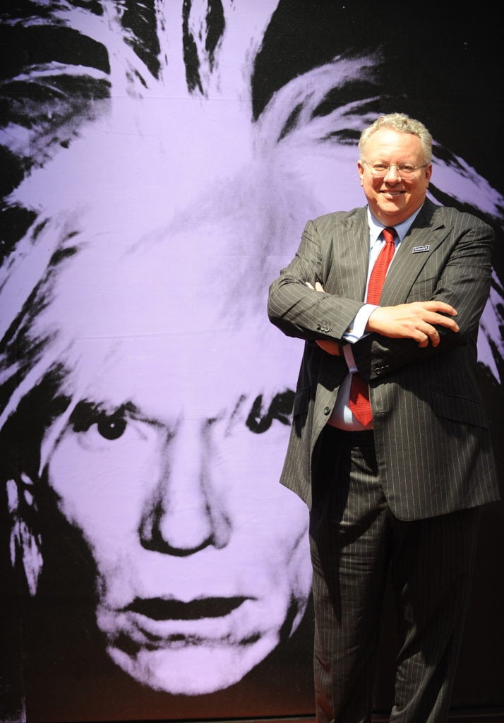 Former Sotheby's CEO Bill Ruprecht next to an Andy Warhol self-portrait from from 1986. (Photo credit: MIKE CLARKE/AFP/Getty Images)