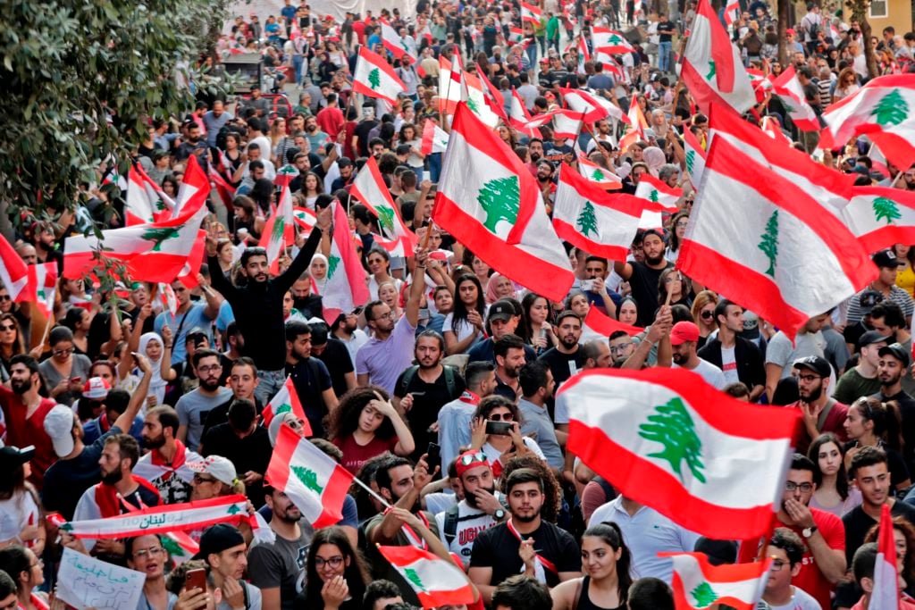 Lebanese protesters wave national flags during demonstrations to demand better living conditions and the ouster of a cast of politicians who have monopolised power and influence for decades, on October 21, 2019 in downtown Beirut. Photo: Anwar Amro/AFP via Getty Images.