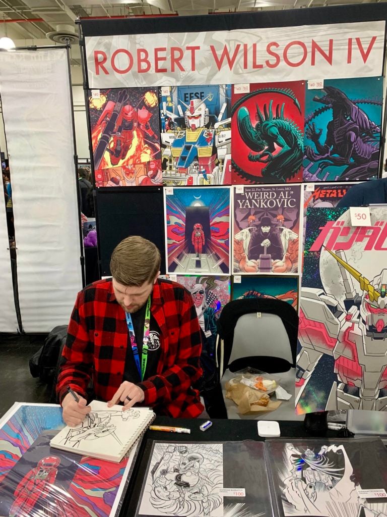 Robert Wilson IV draws at his booth in Artist Alley at New York Comic Con. Photo by Sarah Cascone. 