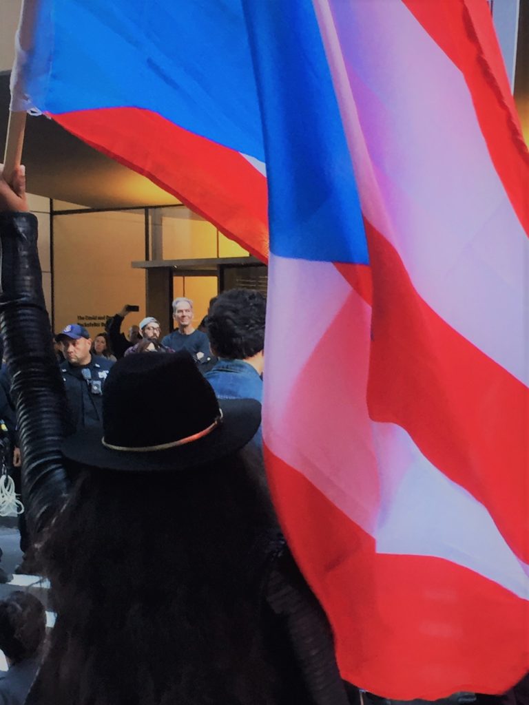 A protester unfurls the Puerto Rican flag in front of MoMA as part of a protest against trustee Steven Tananbaum on October 21. Image: Eileen Kinsella.