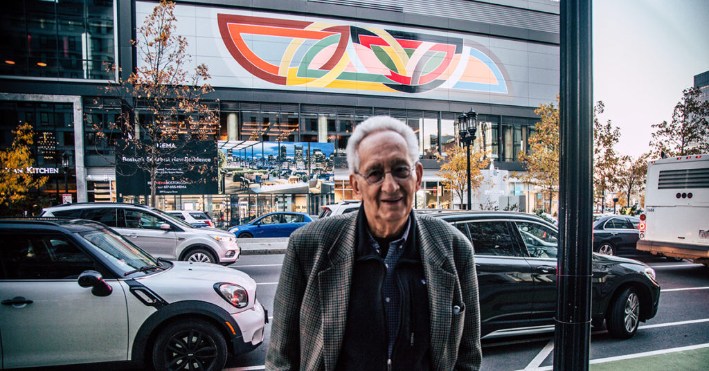 Frank Stella standing in front of the mural of his Damascus Gate (Stretch Variation I) 1970 at the Boston Seaport. 