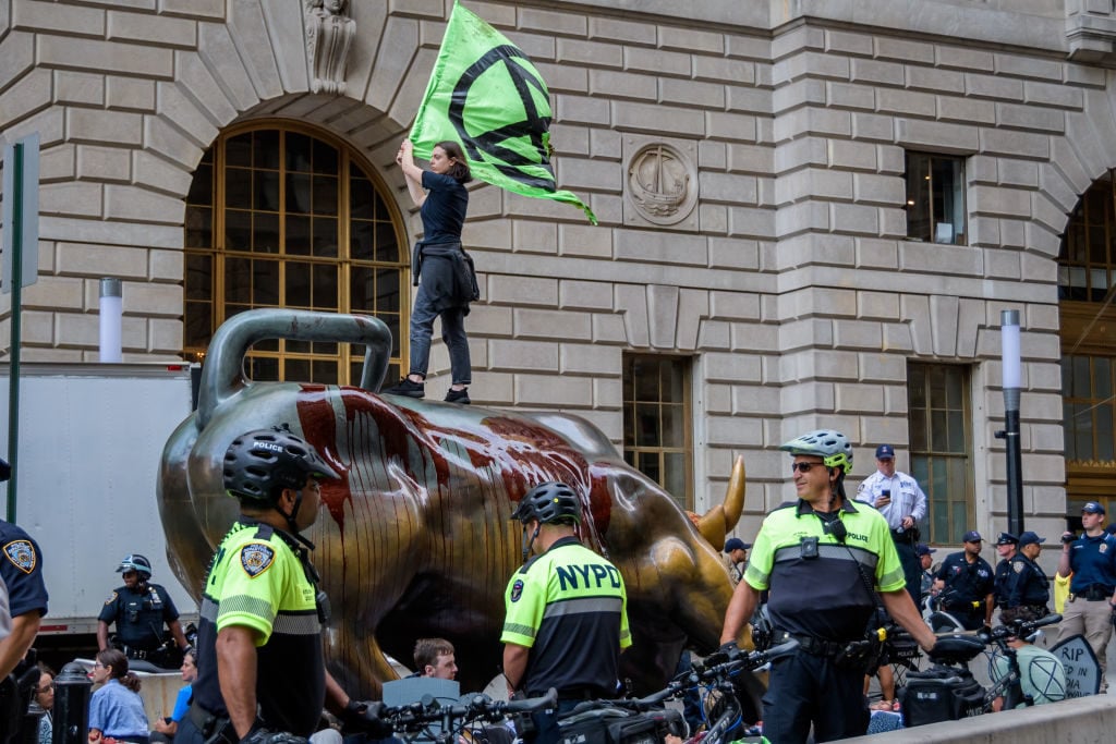 An Extinction Rebellion protester stands on top of the Wall Street Bull. Photo: Erik McGregor/LightRocket via Getty Images.