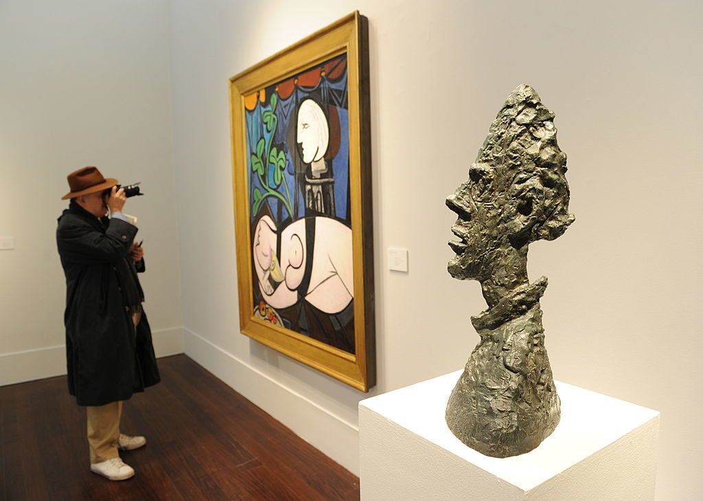 A man photographs Pablo Picasso's Nude, Green Leaves and Bust (1932), next to Alberto Giacometti's Grande tete mince in 2010 at Christie's in New York. Photo by Stan Honda/AFP via Getty Images.
