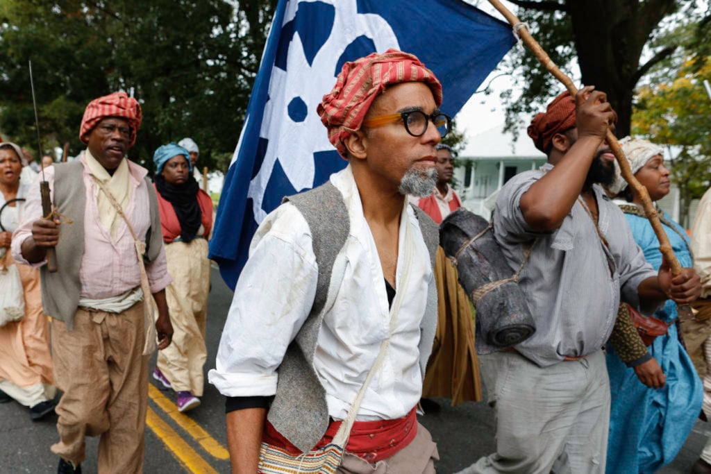 Dread Scott leading the "army of the enslaved" making their way across the 26-mile path through Louisiana. Costumes designed by Alison Parker, Photo: Soul Brother. Courtesy of SRR.