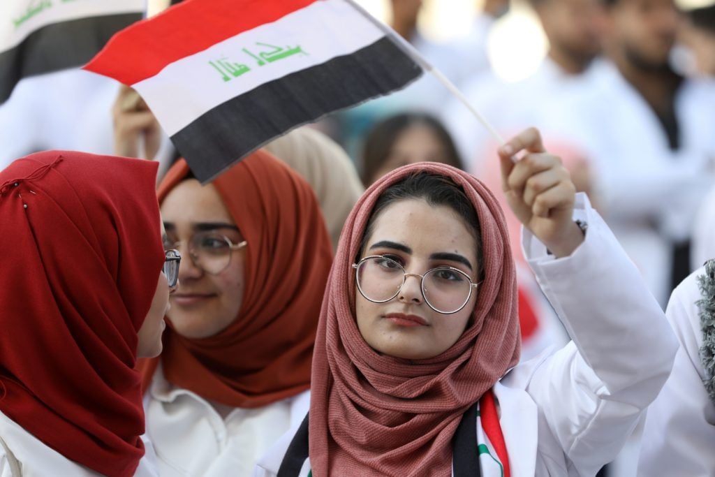 An Iraqi medical student waves the national flag as she takes part in an anti-government protest amid ongoing student strikes at the campus of the university of Basra, in the eponymous southern city on November 12, 2019. Photo by Hussein Faleh/AFP via Getty Images.
