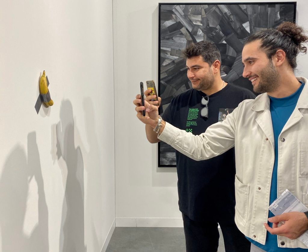 Fairgoers take pictures of Maurizio Cattelan's Comedian, for sale from Perrotin at Art Basel Miami Beach. Photo by Sarah Cascone.