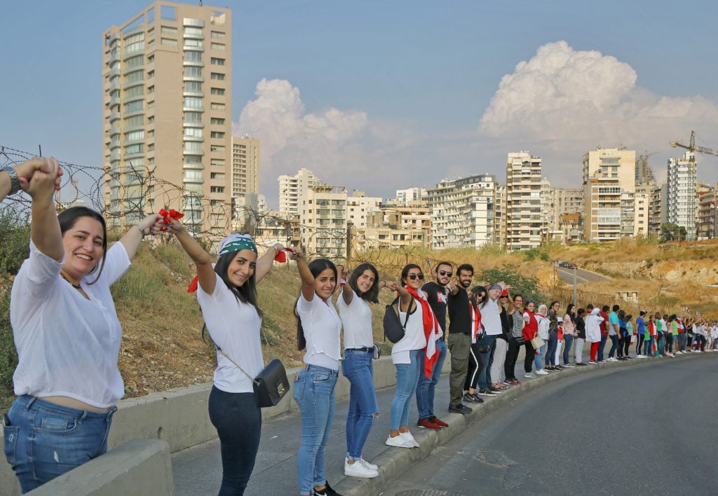 Lebanese people hold hands as they form a human chain stretching along the coast from the capital Beirut to northern and southern Lebanon, symbolizing national unity, during anti-government protests across Lebanon. Photo by Marwan Naamani/picture alliance via Getty Images.