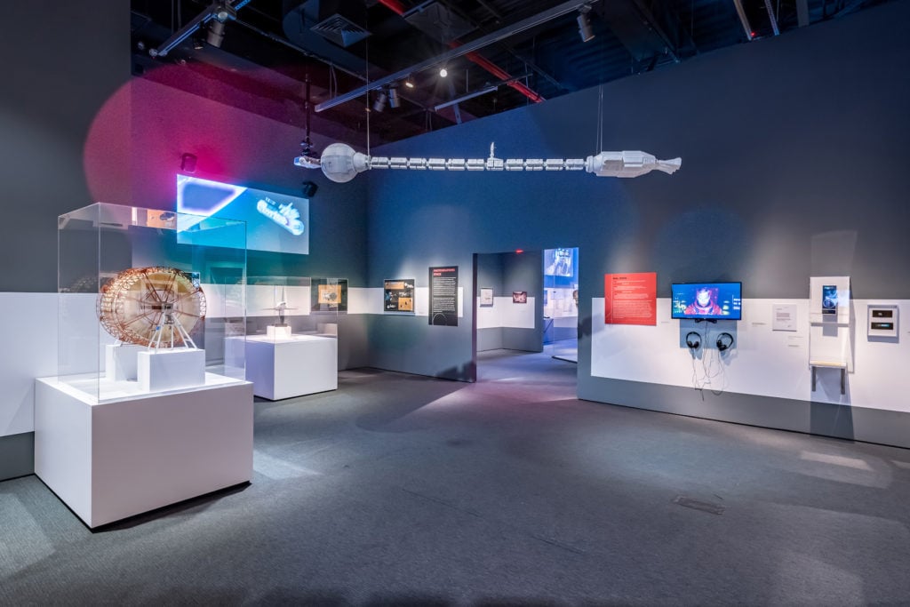 "Envisioning 2001: Stanley Kubrick's Space Odyssey," on view at Museum of the Moving Image. A model of the Discovery One space ship hangs above a gallery. To the left is a model of the Discovery centrifuge set, designed by Harry Lange. Credit: Photo: Thanassi Karageorgiou / Museum of the Moving Image.