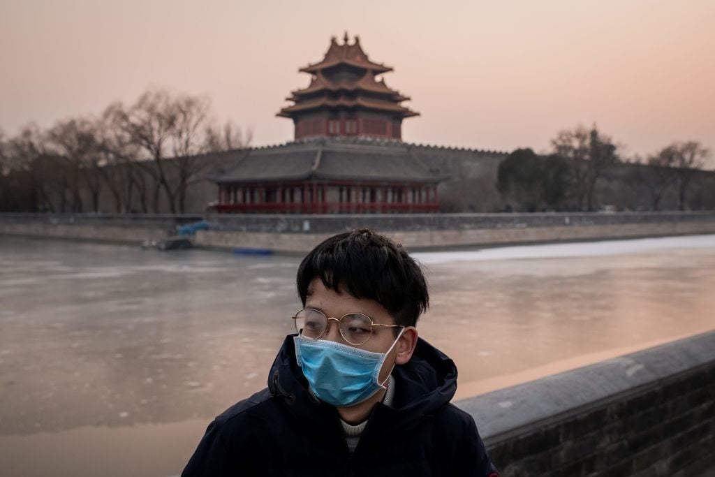 A man wearing a protective facemask to help stop the spread of a deadly SARS-like virus which originated in the central city of Wuhan outside the Forbidden City (in background) in Beijing. - Photo by Nicolas Asfouri/AFP via Getty Images.