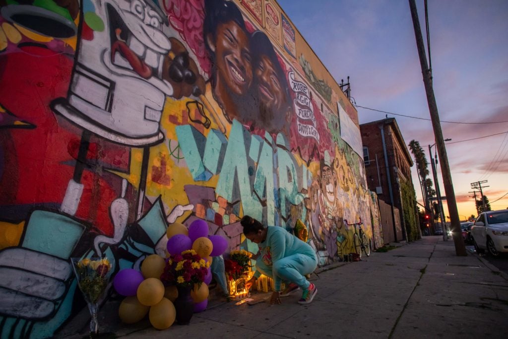 Emily Garbutt lights a candle below a Los Angeles mural by the artists Muck Rock and Mr79lts showing Kobe Bryant and his daughter Gianna Bryant, who were killed with seven others in a helicopter crash on January 26. Photo by Apu Gomes/AFP/Getty Images.