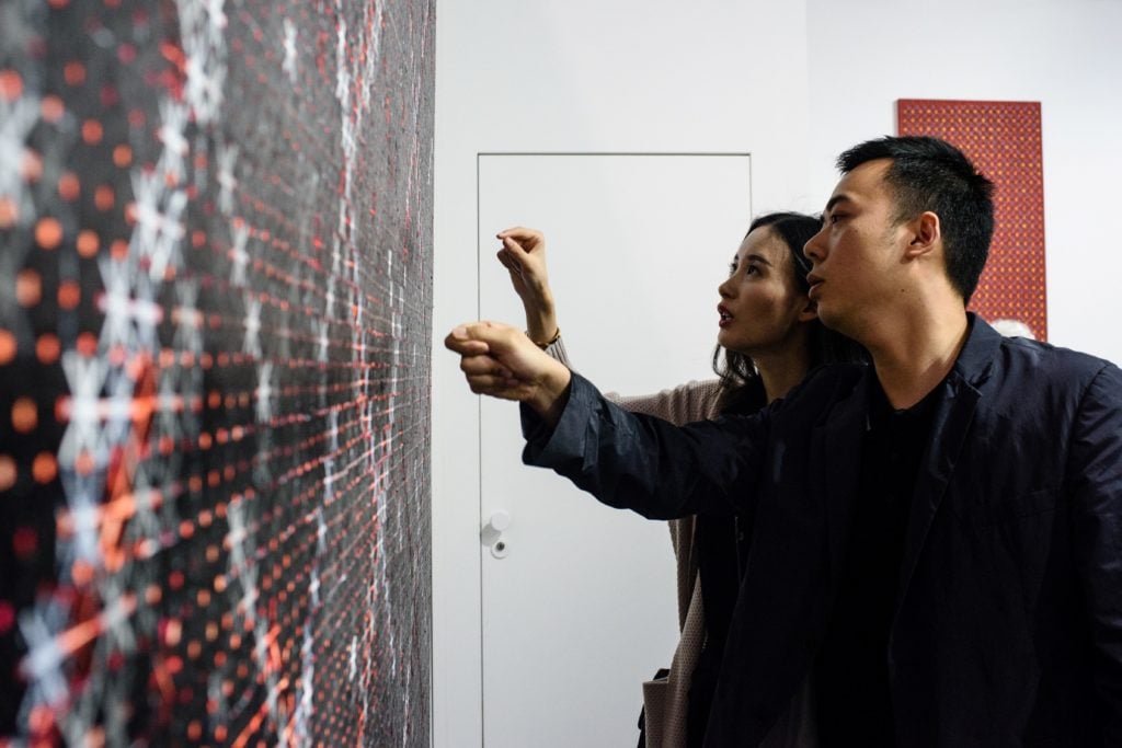 Chinese investment banker Huang Xiaoshuai, 26, and his wife, Wei Mengyuan, in front of their newly acquired painting <i>Appearance of Crosses 2016-12</i> by Chinese artist Ding Yi at Art Basel in Hong Kong in 2017. (ANTHONY WALLACE/AFP via Getty Images)