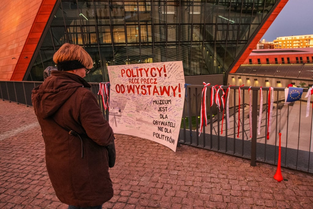 A protester standing in front of a banner that reads “Politicians—Hands off! of the exhibition” in April 2017 in Gdansk, Poland, the same day the Supreme Administrative Court ruled on the de facto liquidation of the World War II Museum and a change in its director. (Photo by Michal Fludra/NurPhoto via Getty Images)