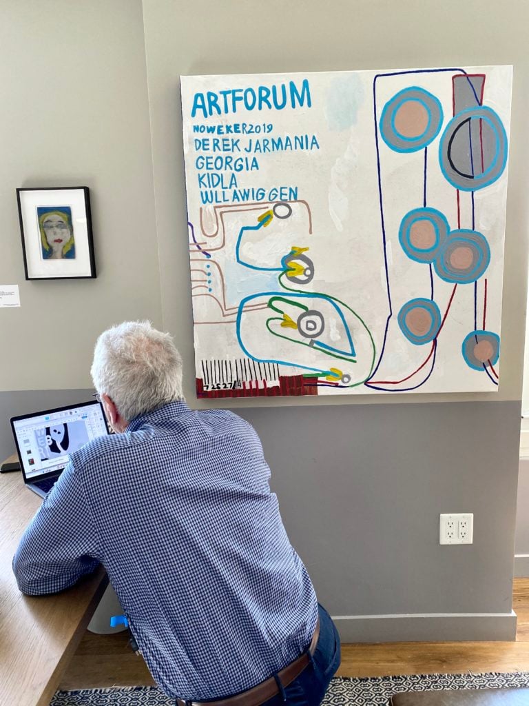 David Hoberman peruses a PDF of available works by self-taught artist Marlon Mullen (also responsible for the large painting to Hoberman's right) inside Adams and Ollman's booth at Felix 2020. Photography by Tim Schneider.