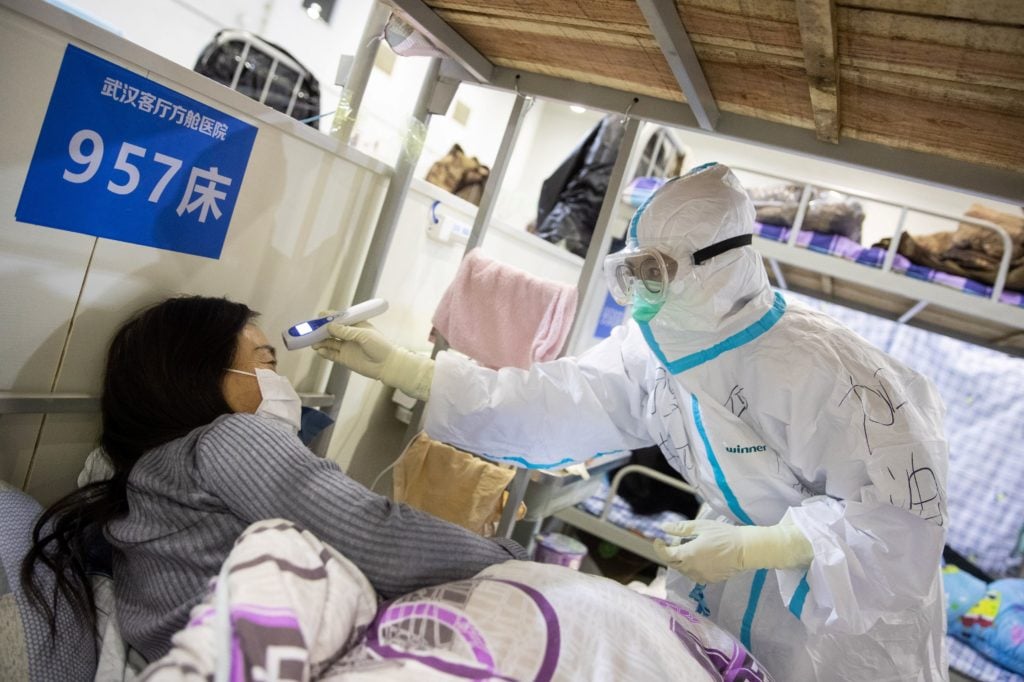 A medical staffer in China checking the body temperature of a patient who has displayed mild symptoms of the COVID-19 coronavirus, at an exhibition center converted into a hospital in Wuhan. Photo by STR/AFP/China OUT via Getty Images.