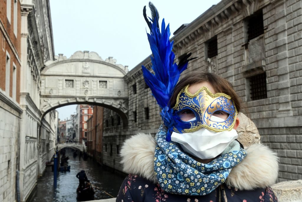 A young tourist wearing a protective facemask and a Carnival mask visits Venice. Photo by Andrea Pattaro/AFP via Getty Images.