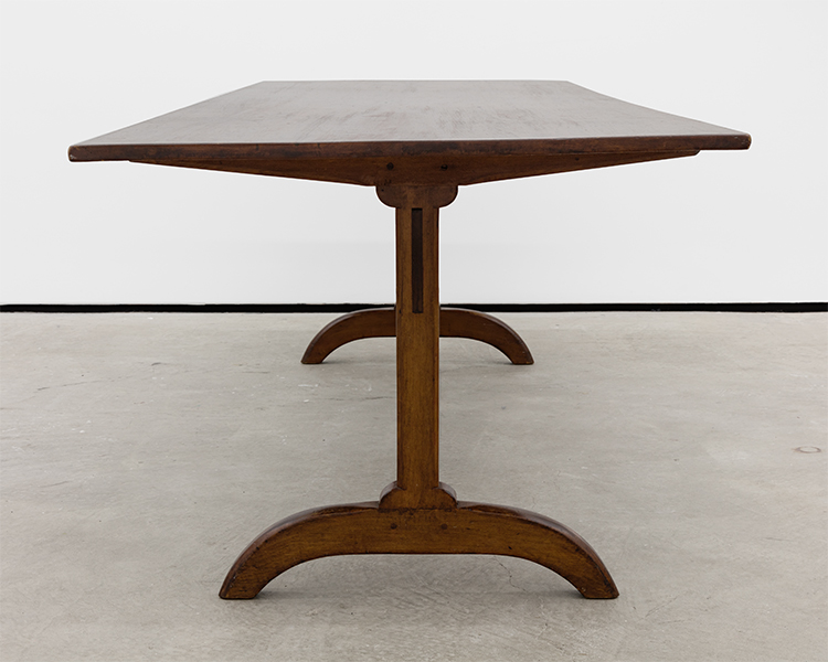 Shaker Trestle Table (ca. 1840). Likely Watervliet, New York. A rare example of a classic Shaker trestle table having a two board top above two beveled tapering cleats supported by carved standards mortised into an arched footed base. Image courtesy Essex Street Gallery.