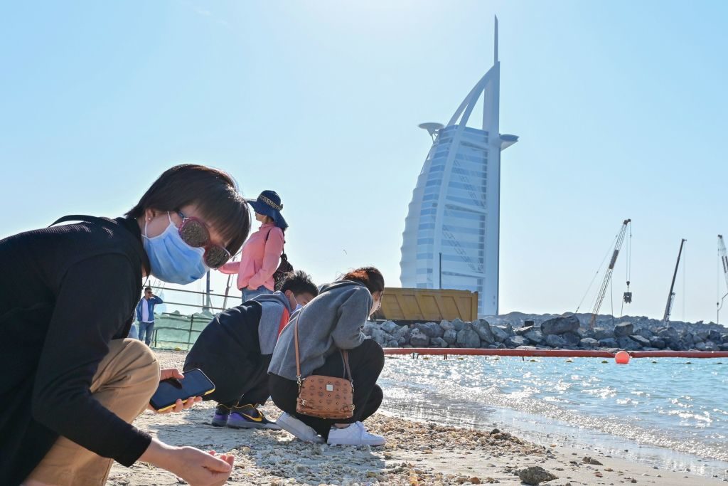 Tourists wearing surgical masks on a beach next to Burj Al Arab in Dubai. Photo by GIUSEPPE CACACE/AFP via Getty Images.