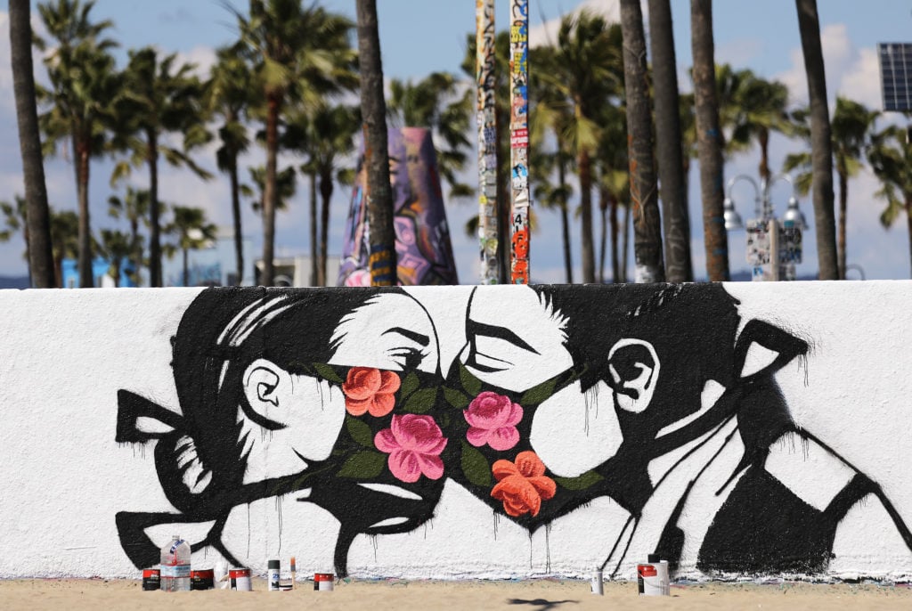 A coronavirus street art work by Pony Wave depicting two people kissing while wearing face masks on Venice Beach. Photo by Mario Tama/Getty Images.